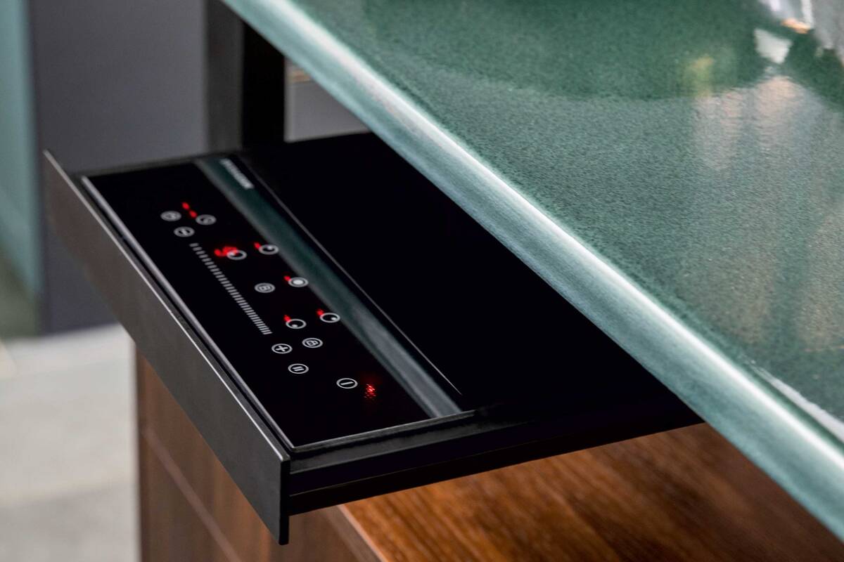 Aussergewöhnlich: Die Arbeitsplatten aus robustem Lavagestein sind zugleich Induktionskochfelder, die schnell aufheizen und auch rasch wieder abkühlen. Die Bedienung erfolgt über ein ausziehbares Tableau. Elbau Küchen AG.