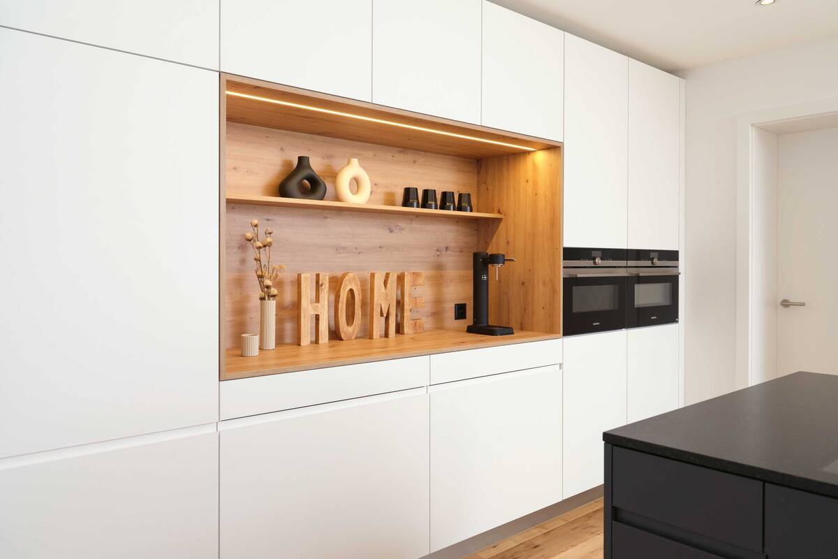 In der weissen Hochschrankfront mit Vorratsschrank, Kühlschrank und den beiden Geräteschränken mit Backofen/Steamer und Backofen/Mikrowelle wird die Kaffeenische mit der integrierten Beleuchtung zum Blickpunkt. Loosli AG.