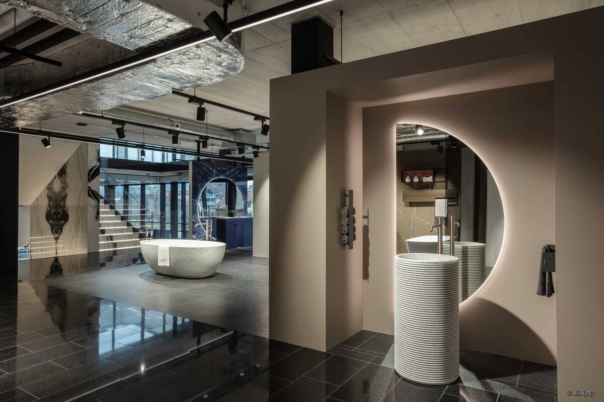 Die bodenstehende Waschtischsäule «Introverso» von Antonio Lupi ist aus dem edlen Marmor Bianco Carrara gefertigt. Ein besonderes Highlight ist der beleuchtete Spiegel «Spicchio» mit seiner Halbmondform. Hans Eisenring Natursteinwerk.