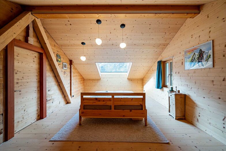 Das Elternschlafzimmer mit dem grossen Dachfenster ist klar, schlicht und dennoch Luxus pur. Abends unterm Sternenhimmel einschlafen und sich morgens vom Sonnenlicht wachkitzeln lassen – das ist wahrhaftig ein Traum.