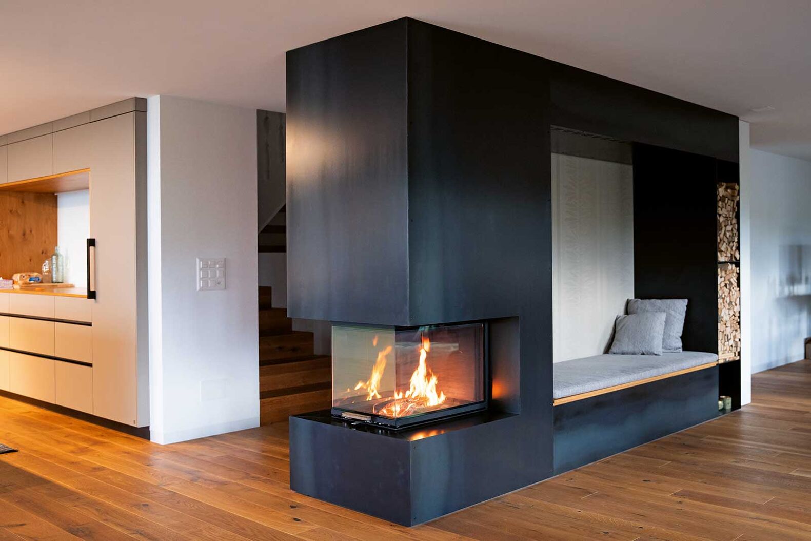 Besonders bei Cheminées als Raumtrenner kann man bei der individuellen Gestaltung richtig kreativ werden. Eine Feuerholzaufbewahrung ist natürlich sehr praktisch, doch nicht die einzige Option, wie der Korpus genutzt werden kann. Eine Sitznische wie bei diesem Cheminée lässt das Element weniger massiv erscheinen und lädt zum gemütlichen Verweilen ein. Hans Greub AG, www.hans-greub.ch
