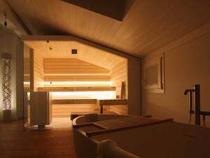 Die Sauna und die Sitzbänke wurden bei diesem Objekt an die Dachschräge angepasst. Eine gemütliche Atmosphäre schafft die indirekte, warmweisse LED-Beleuchtung. Die Glasfront lässt den Raum grosszügig wirken. Ging Saunabau AG.