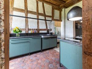 Tradition trifft auf Moderne: In einem Landhaus aus dem 18. Jahrhundert treffen farbig gestrichene Grobspanplatten auf Altholz, das aus dem ursprünglichen Gebäude stammt. Die Küchenabdeckung aus Naturstein unterstützt den rustikalen Stil. Furrer Küchen AG.