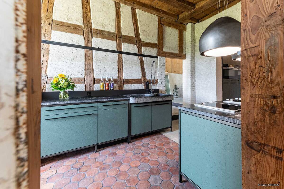Tradition trifft auf Moderne: In einem Landhaus aus dem 18. Jahrhundert treffen farbig gestrichene Grobspanplatten auf Altholz, das aus dem ursprünglichen Gebäude stammt. Die Küchenabdeckung aus Naturstein unterstützt den rustikalen Stil. Furrer Küchen AG.