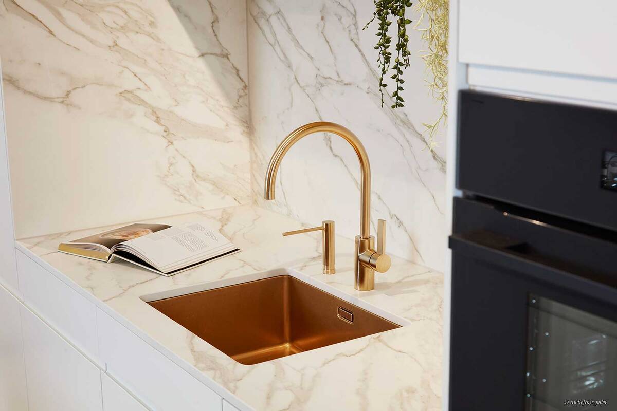 Dieses Küchendesign verbindet elegante, klare Linien mit luxuriösen Akzenten durch goldene Armaturen, die sich schnörkellos in das Gesamtbild einfügen. Sabag AG.