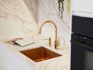 Dieses Küchendesign verbindet elegante, klare Linien mit luxuriösen Akzenten durch goldene Armaturen, die sich schnörkellos in das Gesamtbild einfügen. Sabag AG.