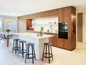 Die Kombination aus Holz und Marmor symbolisiert eine Einheit von Eleganz, Natürlichkeit und Moderne. Das Holz setzt warme Akzente und schafft eine einladende Atmosphäre, während die Kücheninsel aus Marmor durch seine glatte Oberfläche sanft und luxuriös das einfallende Licht reflektiert. Sanitas Troesch AG.